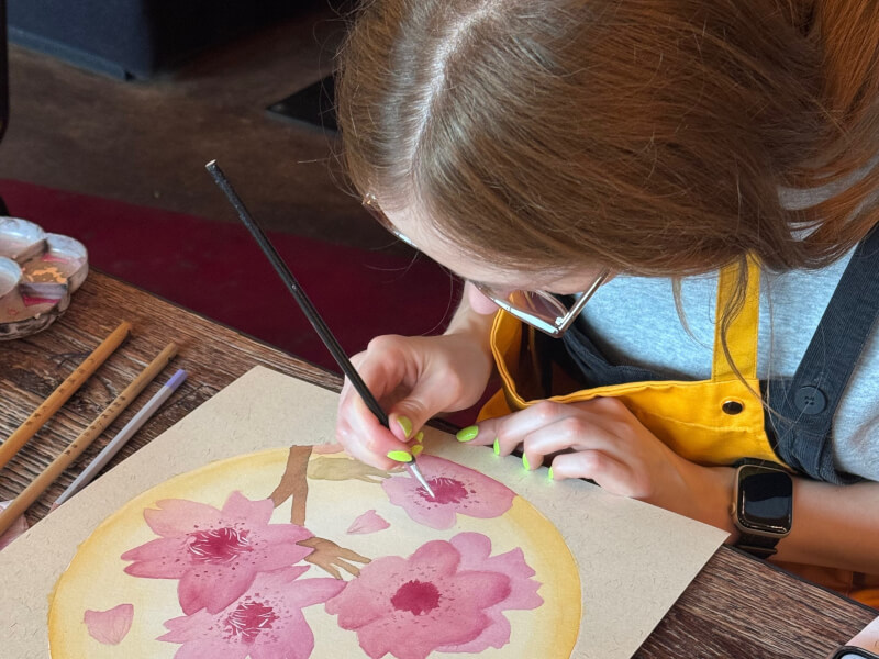 A close up of a person painting a pink floral design onto rice paper